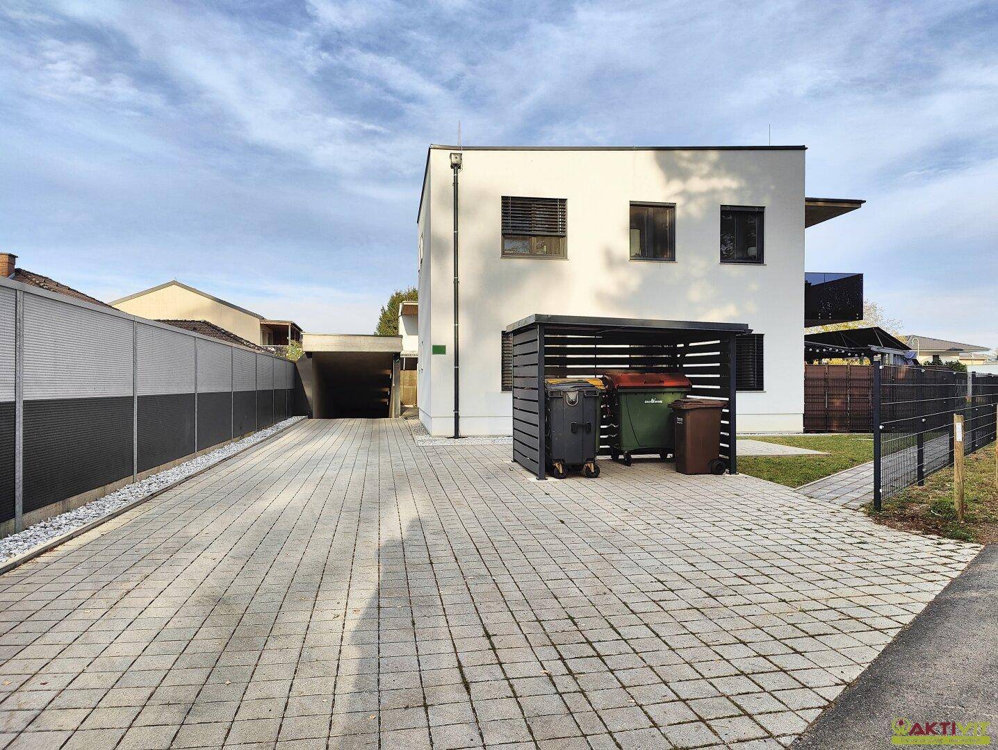 Gebäudeansicht mit breiter gepflasterter Zufahrt und überdachtem Carport-Bereich.