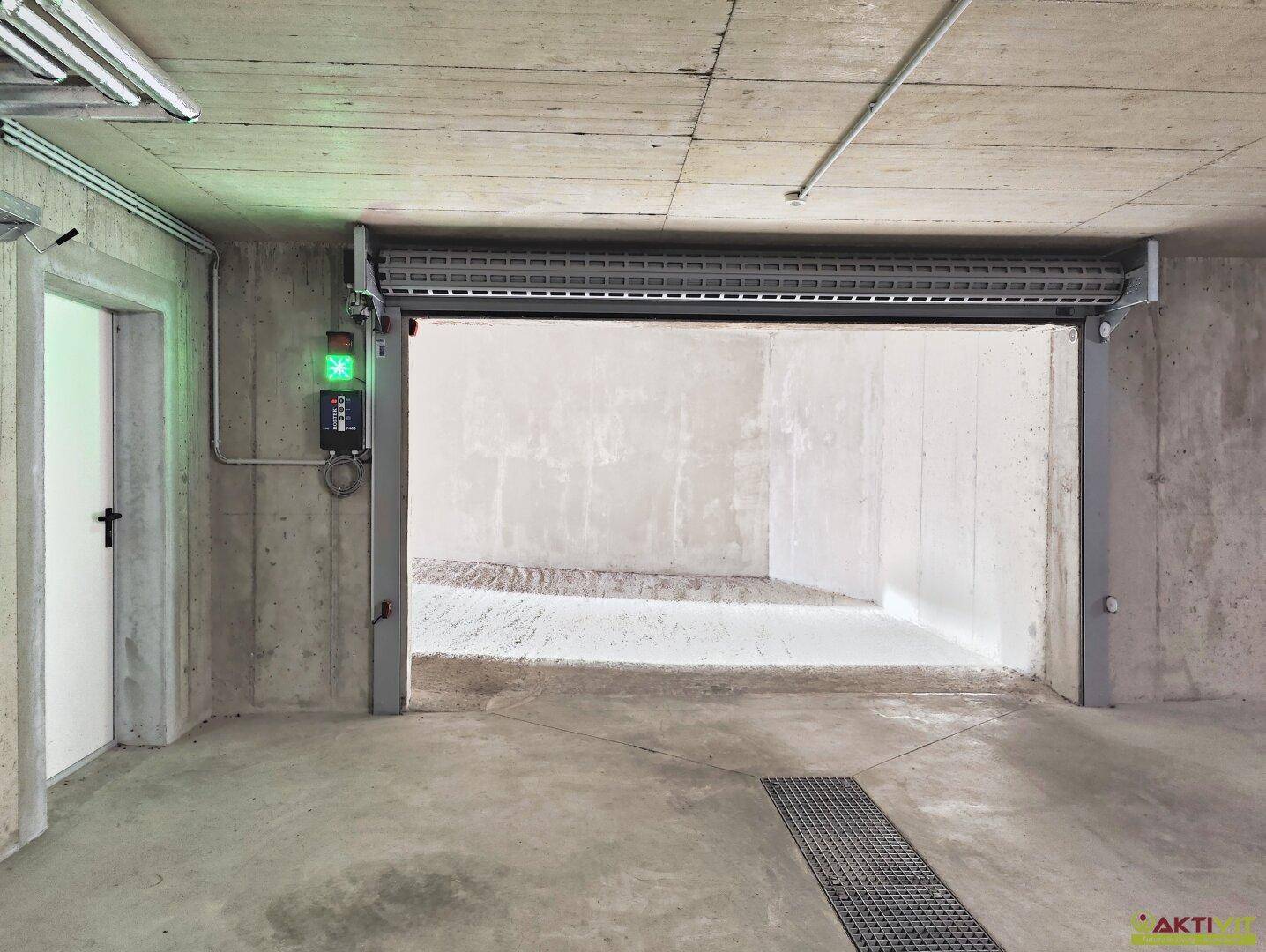 Tiefgarage mit offenem Rolltor, Betonwänden und einem grünen Signallicht für die Einfahrt.