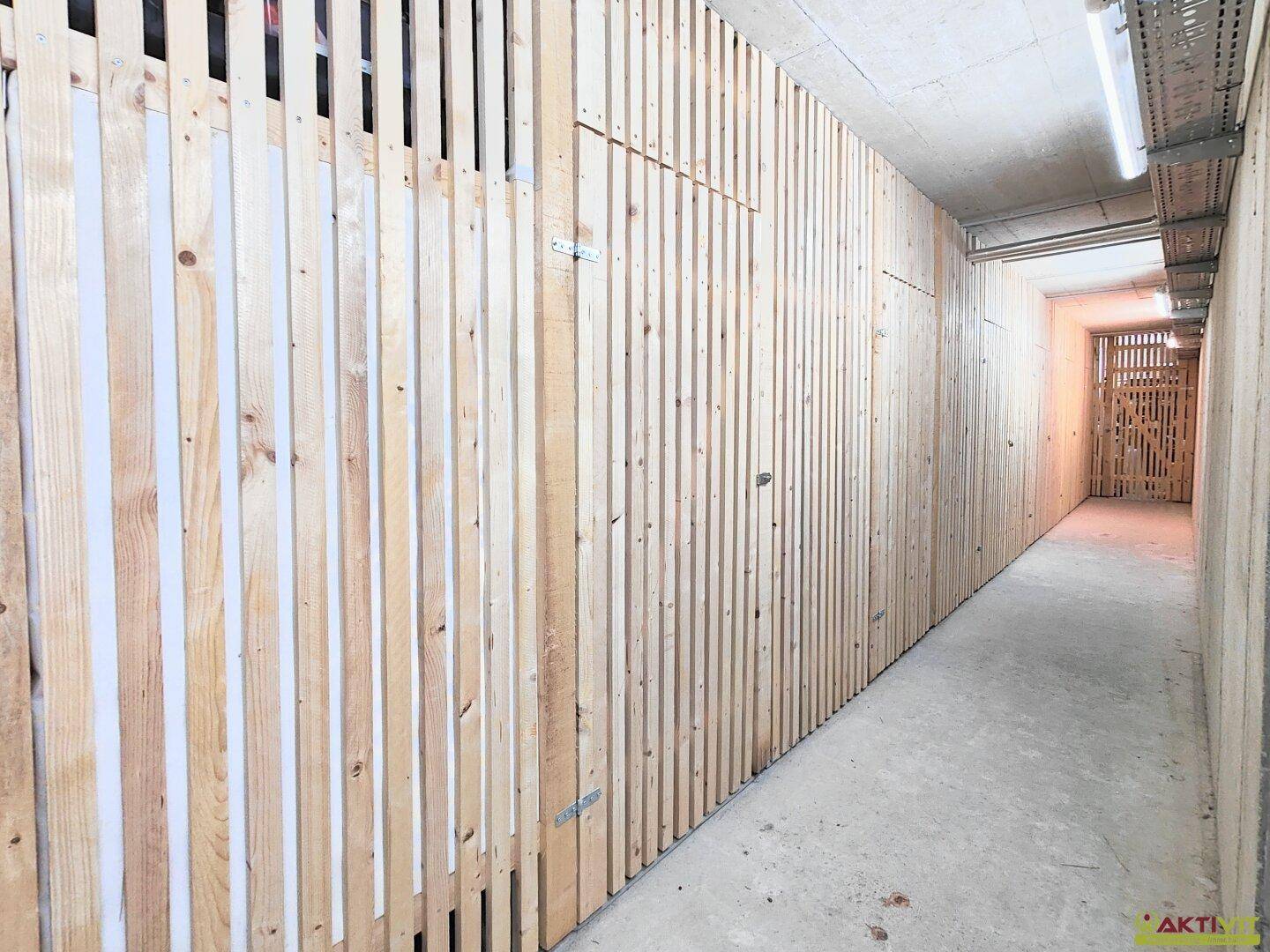 Gang im Untergeschoss mit Reihen von Holzlatten-Abtrennungen für individuelle Lagerräume.