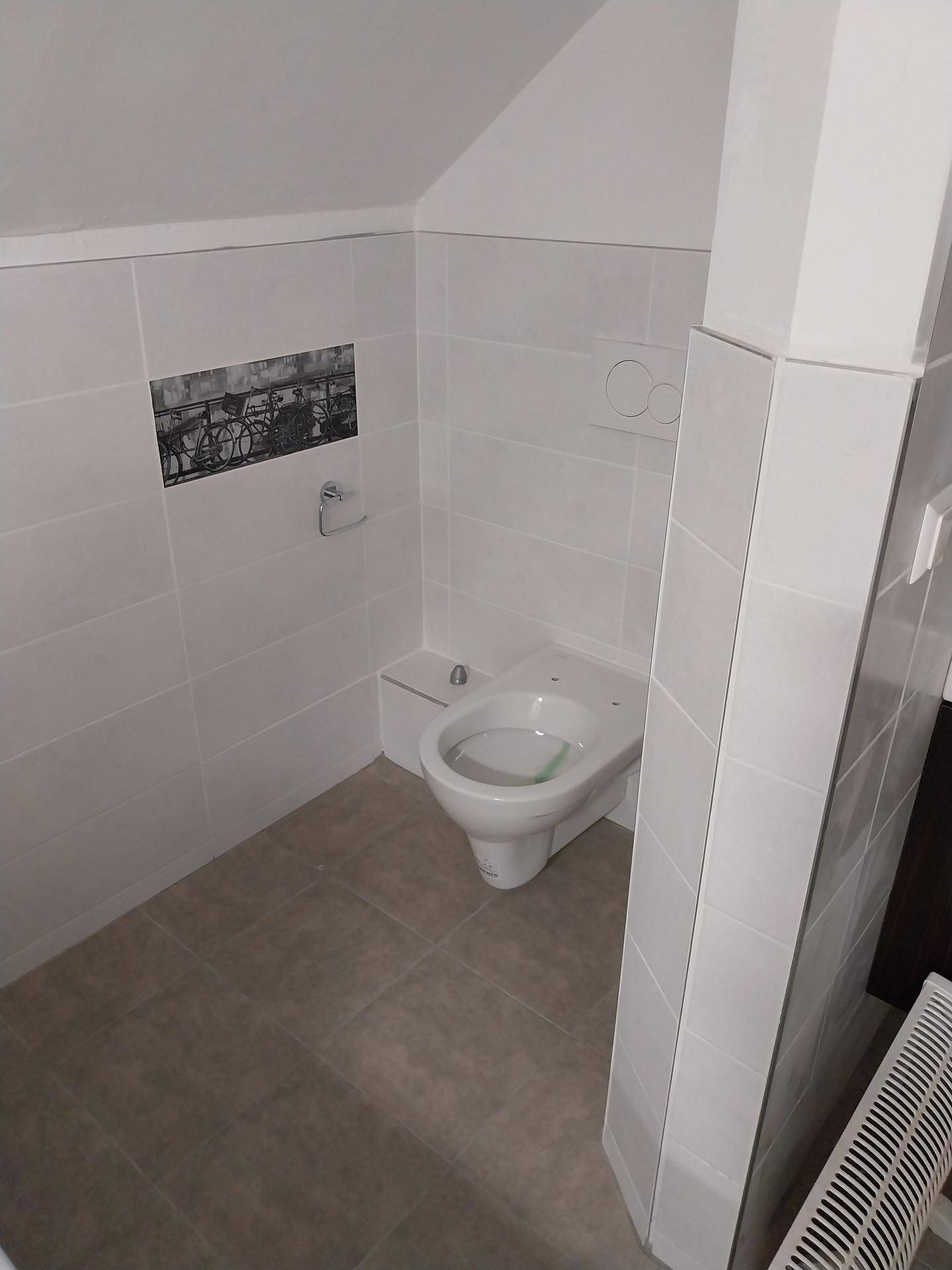 WC-Bereich mit wandhängender Toilette, weißen Fliesen und einer dekorativen Fliesenbordüre unter der Dachschräge.