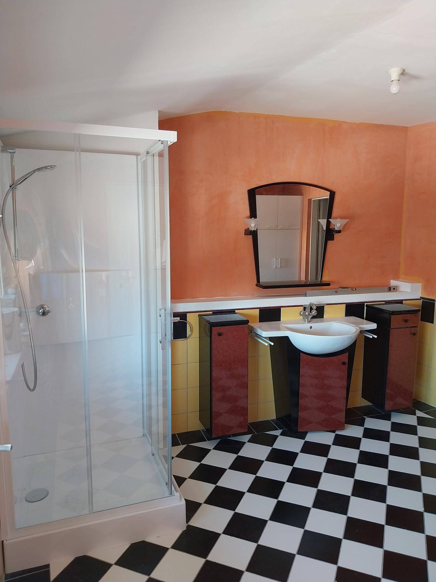 Badezimmer mit markanten schwarz-weiß karierten Fliesen, orangefarbenen Wänden und moderner Waschtischanlage.