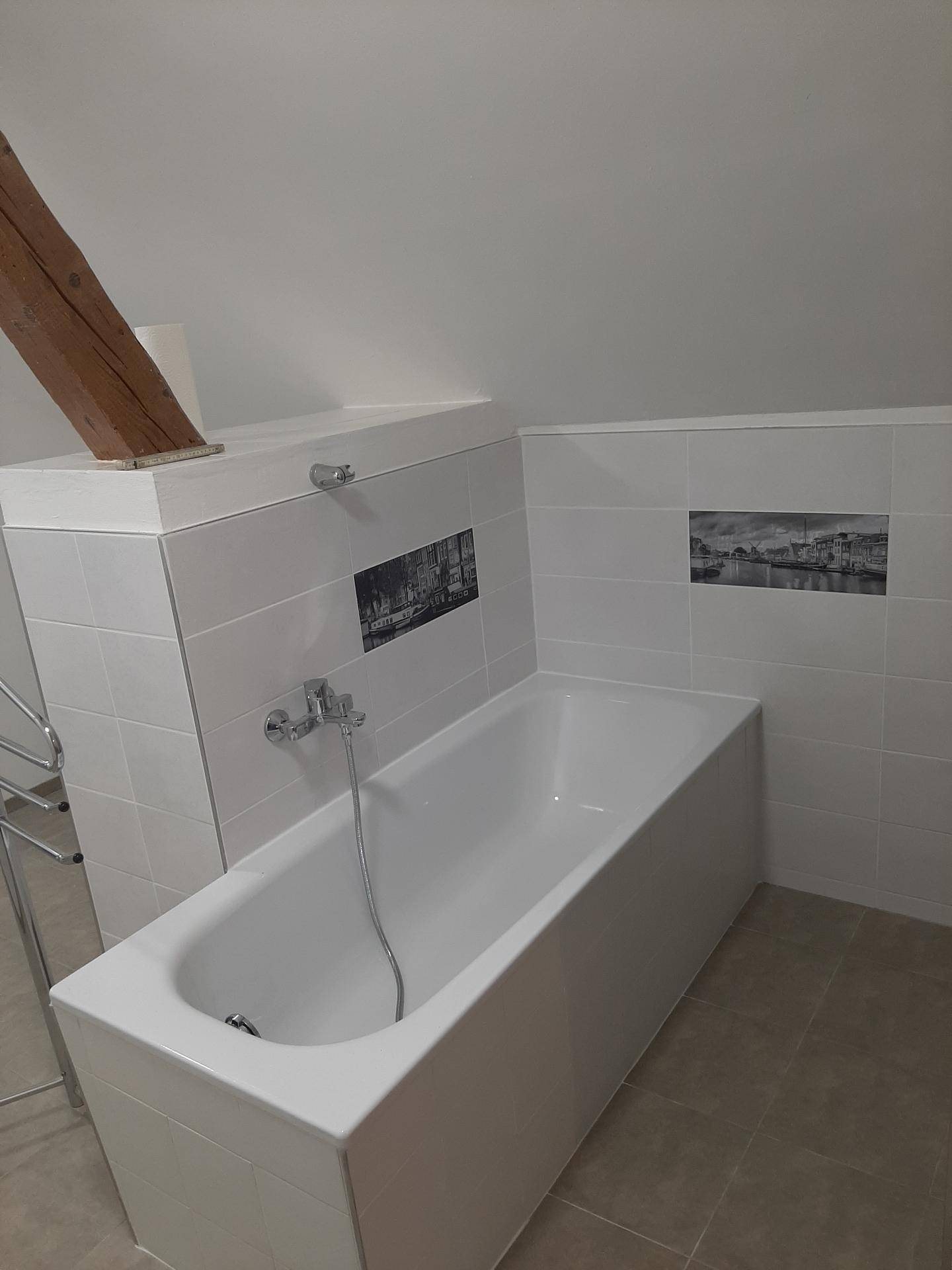 Badezimmer mit eingebauter Badewanne, weißen Fliesen und dekorativen Akzentfliesen unter einem Holzbalken.