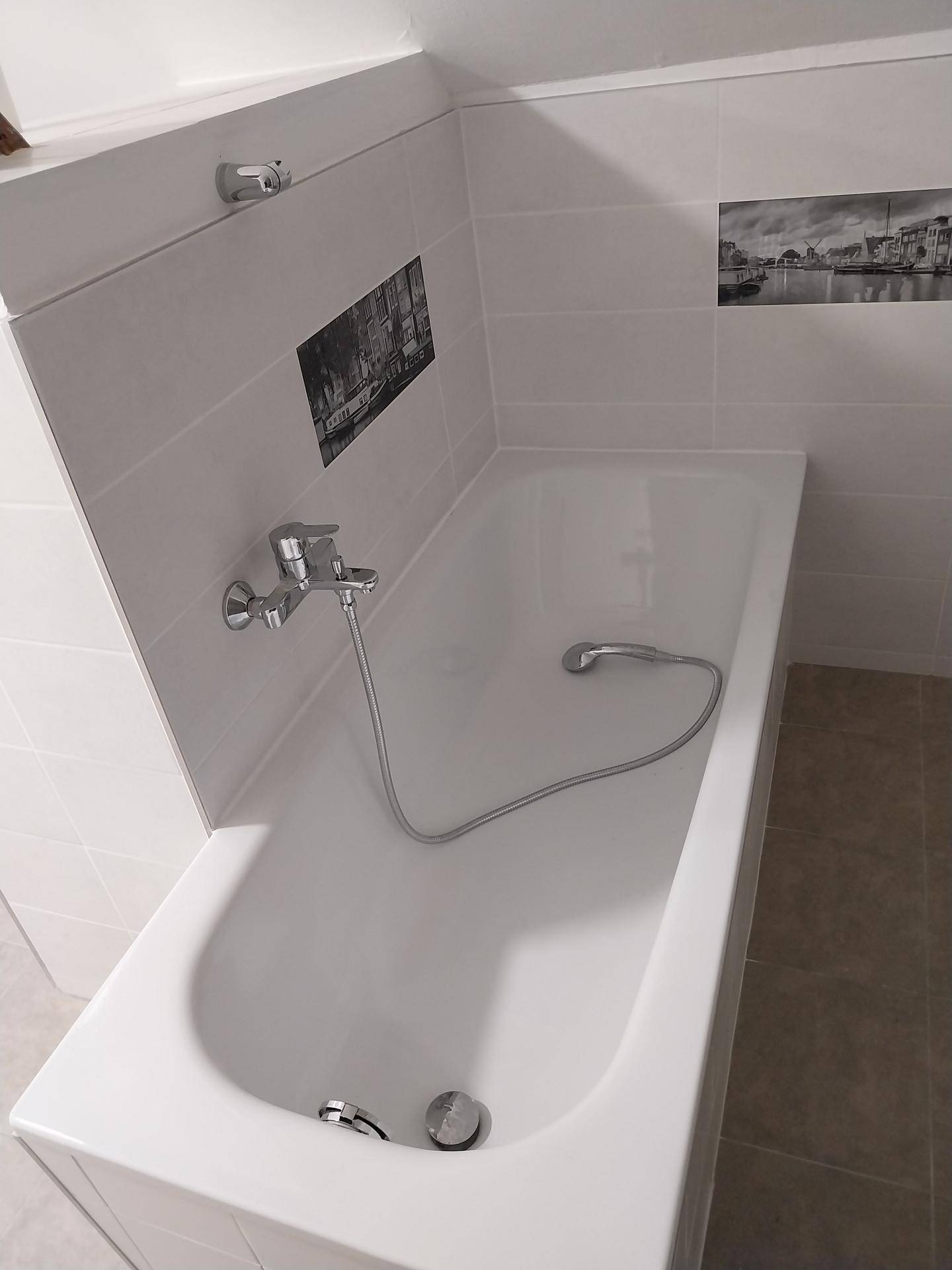 Badezimmer mit eingebauter Badewanne, weißen Fliesen und einer dekorativen Fliesenbordüre unter der Dachschräge.