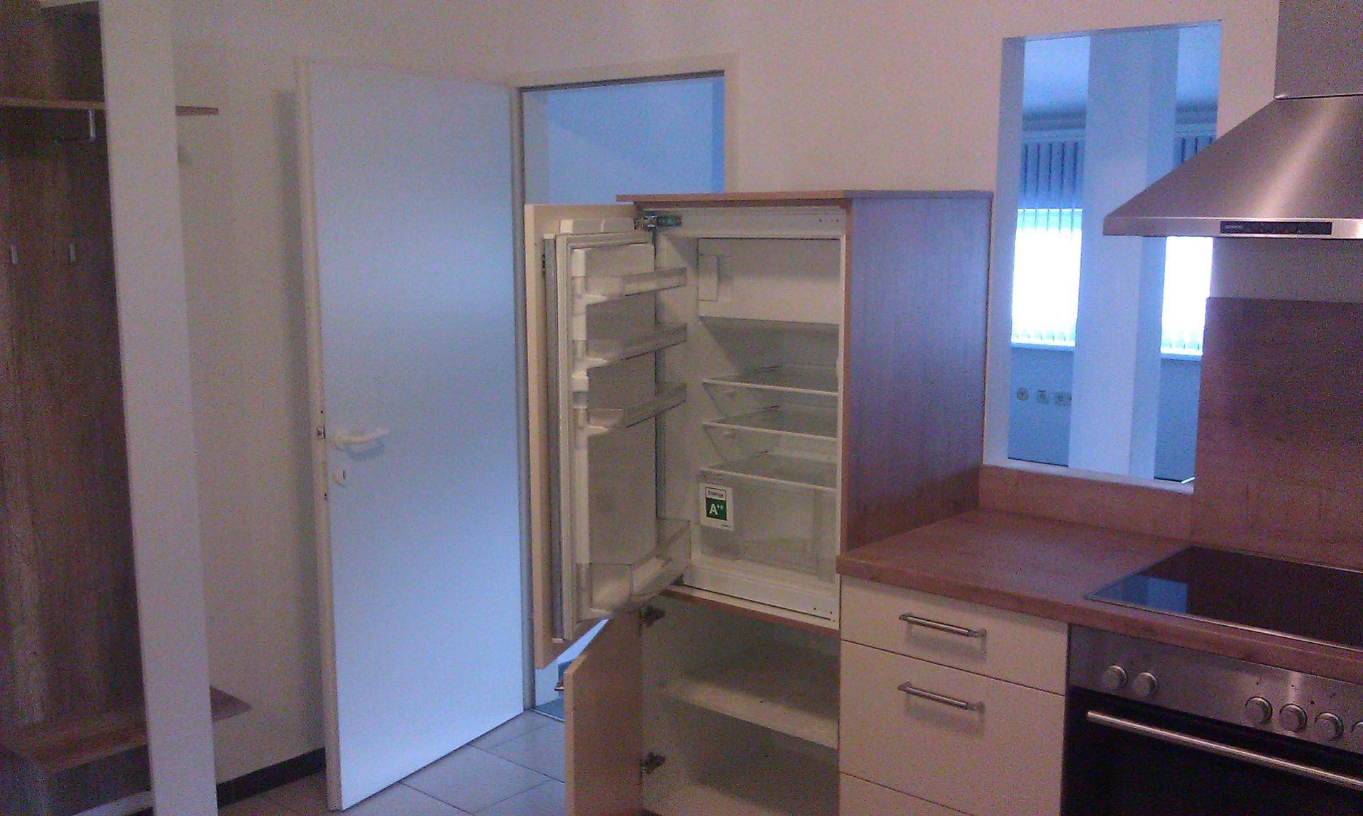 Kleine Einbauküche mit offenem Kühlschrank, Induktionskochfeld und Dunstabzugshaube.
