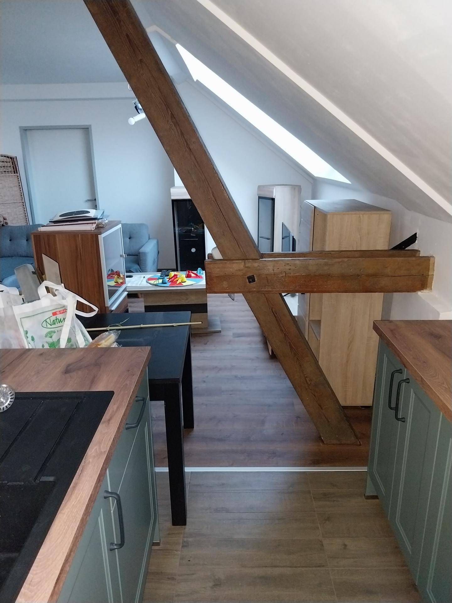 Blick von der Küche in den offenen Wohnbereich mit markantem Holzbalken und schrägen Dachschrägen.