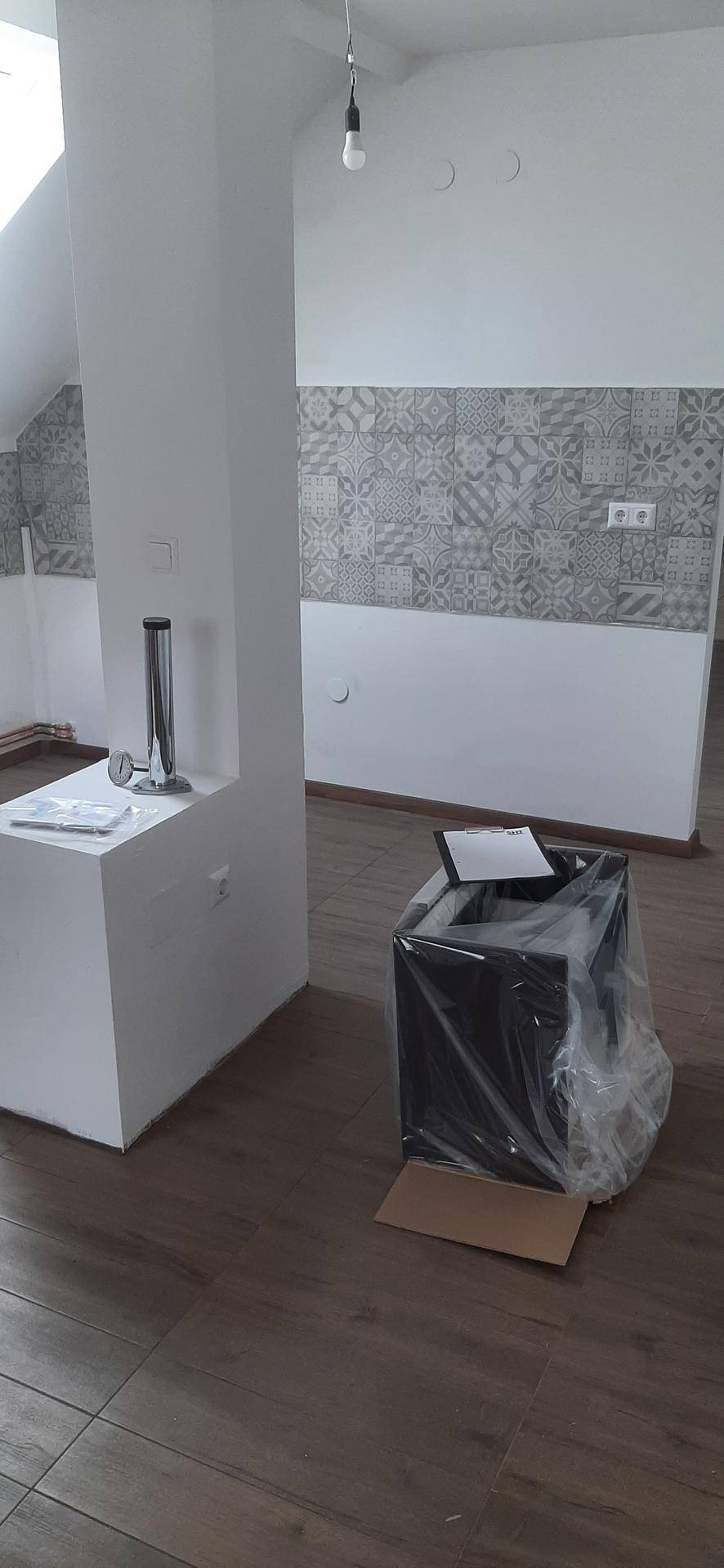 Offener Wohnbereich mit gemusterter Tapete, Laminatboden und einer tragenden Säule, noch im Ausbau.