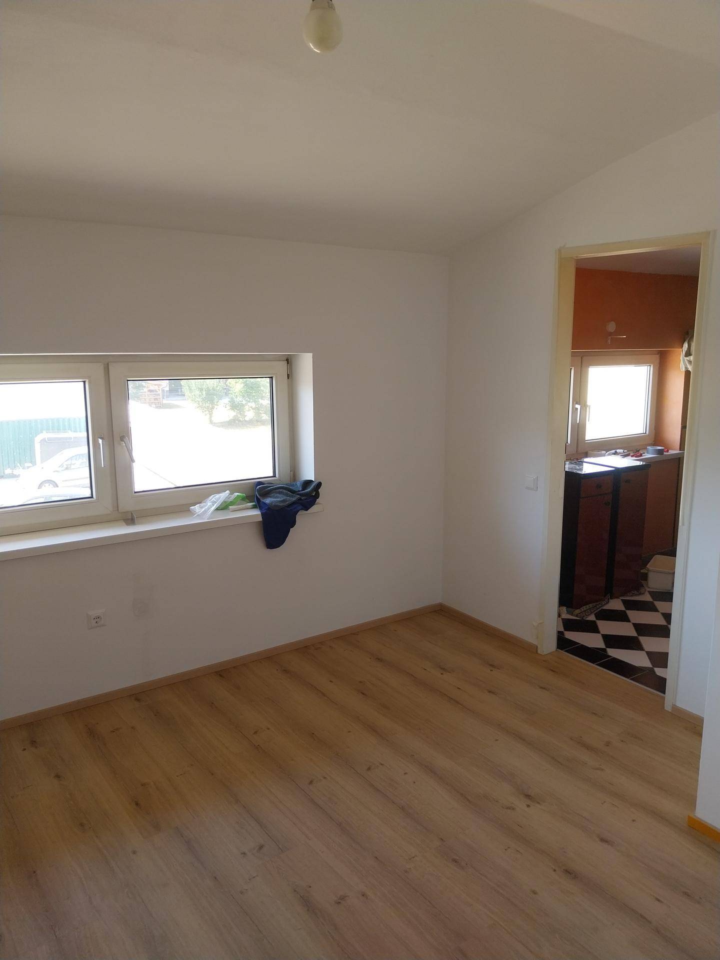 Leerer Raum mit Laminatboden und Fenster, bietet Zugang zu einem angrenzenden Zimmer mit Fliesen.