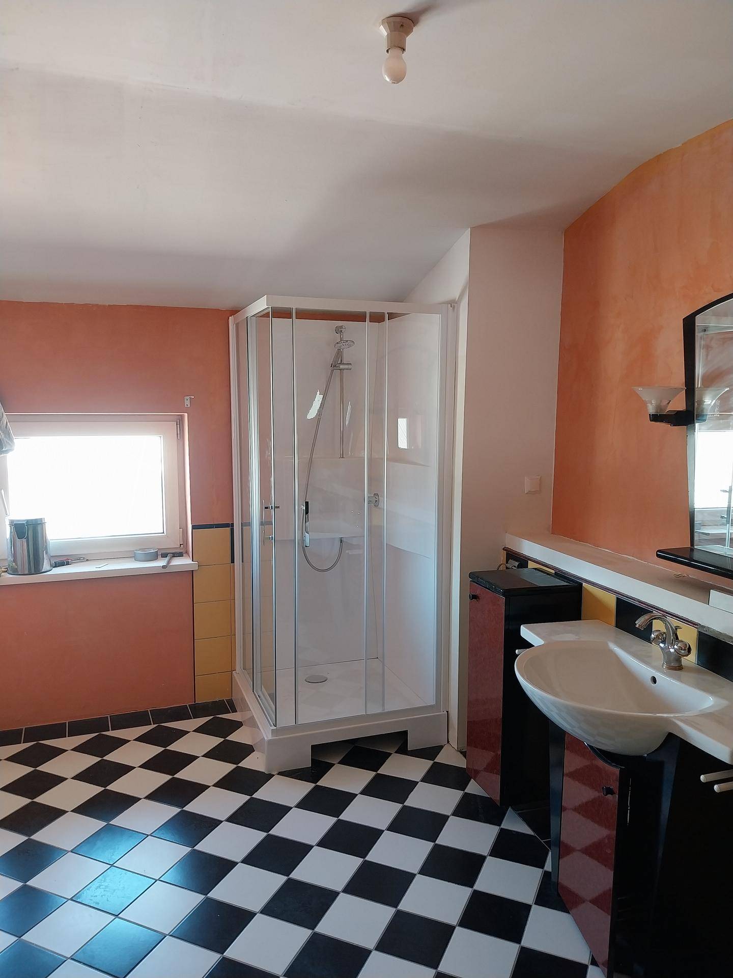 Helles Badezimmer mit Duschkabine, Waschtisch und auffälligem schwarz-weiß kariertem Fliesenboden.