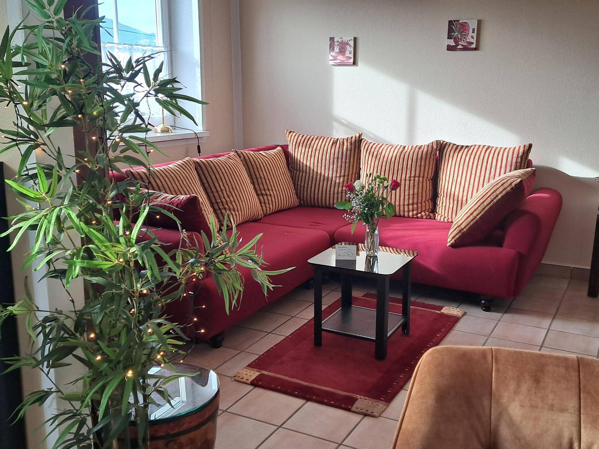 Gemütliches Wohnzimmer mit rotem Ecksofa, Couchtisch und Fliesenboden, hell und einladend.