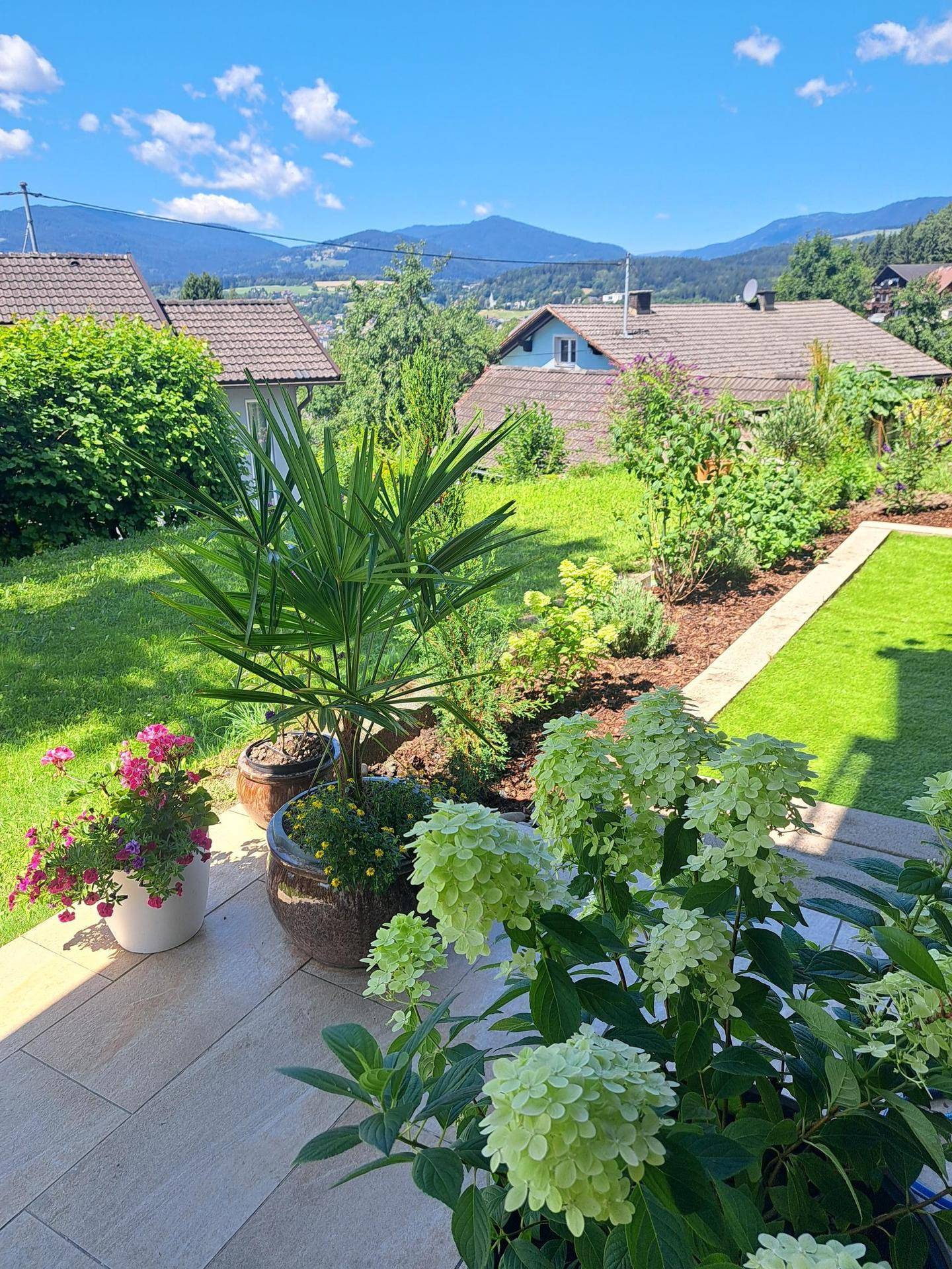 Gepflegter Garten mit Blumenbeeten, Rasenfläche und malerischem Bergblick im Hintergrund.
