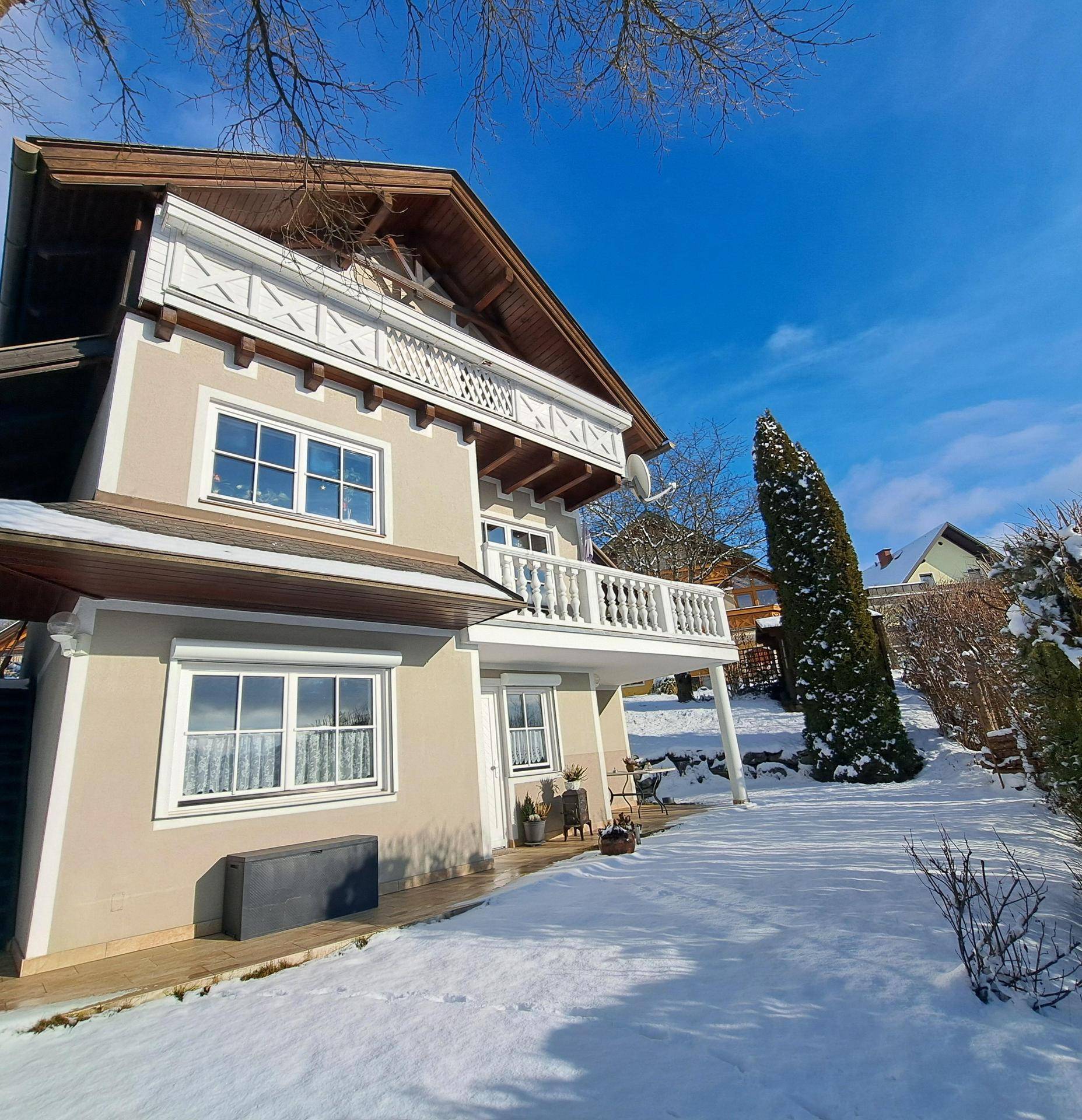 Hausfassade im Winter mit Schnee bedeckt, umgeben von einer idyllischen Winterlandschaft.