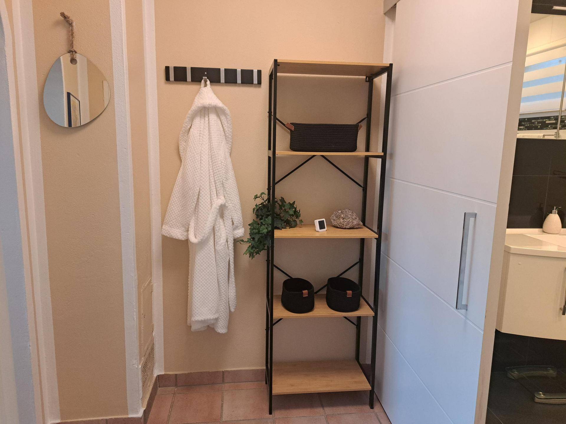 Heller Flur mit Garderobe, Spiegel und Regal, der zum Badezimmer führt.
