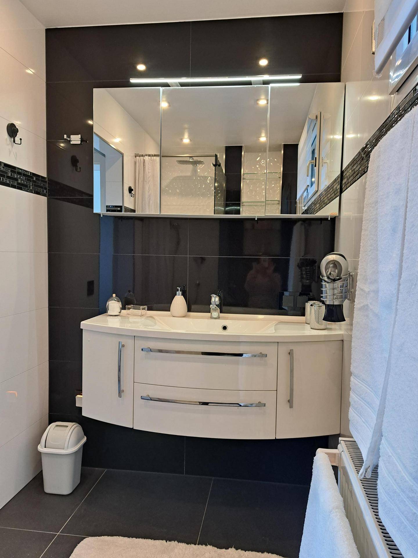 Modernes Badezimmer mit Waschtisch, Spiegelschrank und eleganten schwarz-weißen Fliesen.
