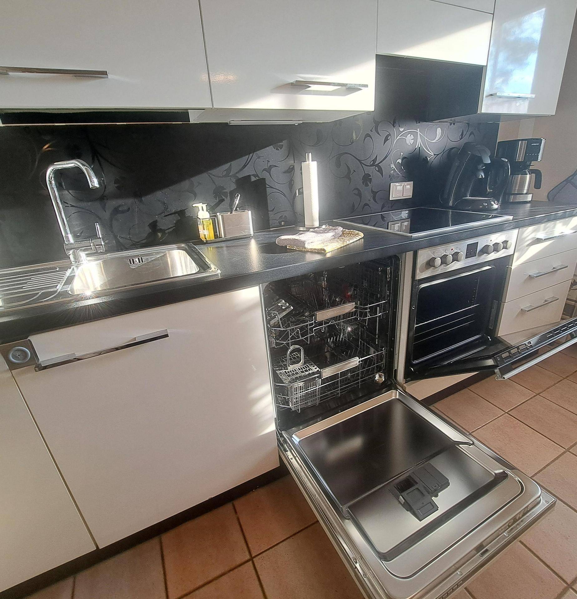 Moderne Einbauküche mit Spülmaschine, Induktionskochfeld und schwarzer Rückwand.