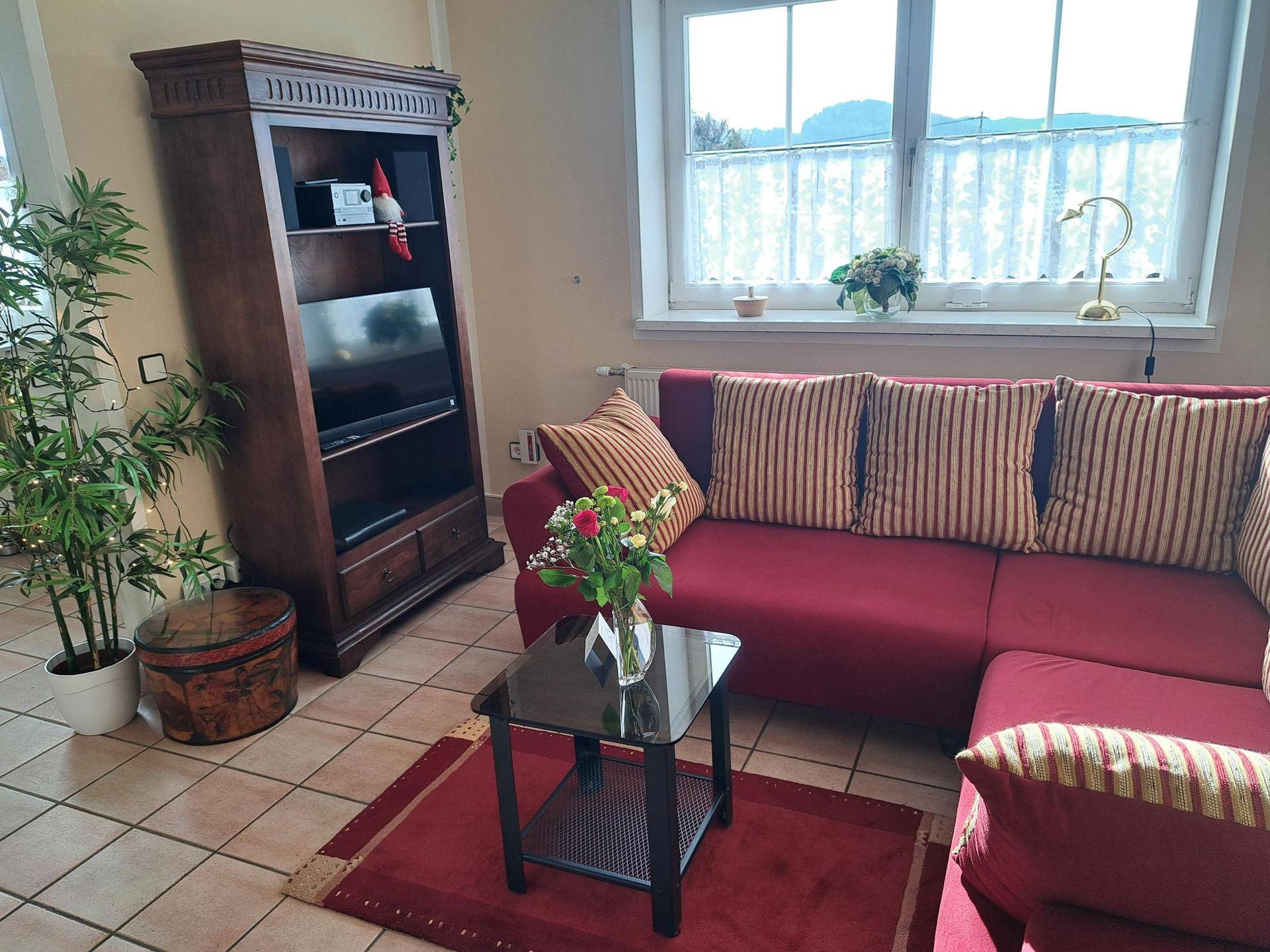 Helles Wohnzimmer mit rotem Sofa, TV-Möbel und Blick ins Grüne durch das Fenster.