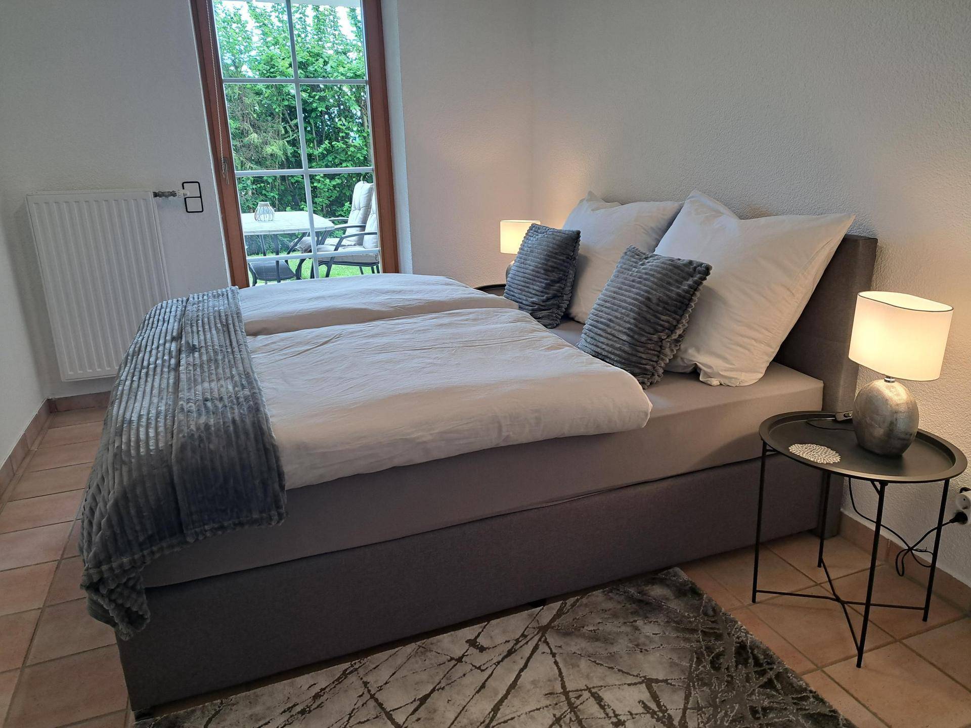 Schlafzimmer mit Doppelbett, Nachttisch und Zugang zu einer kleinen Terrasse oder Balkon.