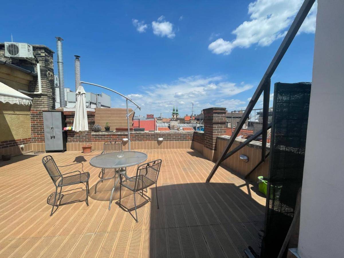 Geräumige Dachterrasse mit Sitzgelegenheiten und weitem Blick über die Stadt unter blauem Himmel.