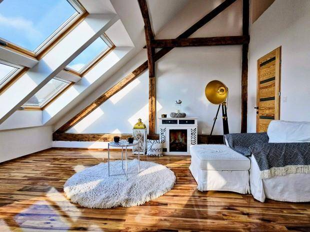Heller Dachgeschoss-Wohnraum mit sichtbaren Holzbalken, großen Dachfenstern und Holzboden.