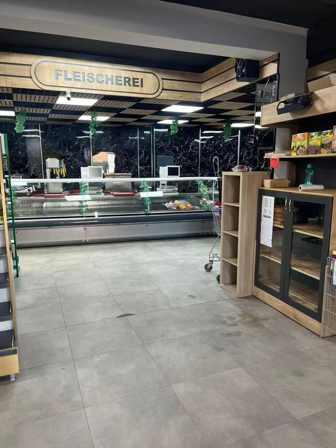 Theke einer Fleischerei in einem modernen Ladengeschäft mit dunklen Wänden, Holzdetails und Fliesenboden.