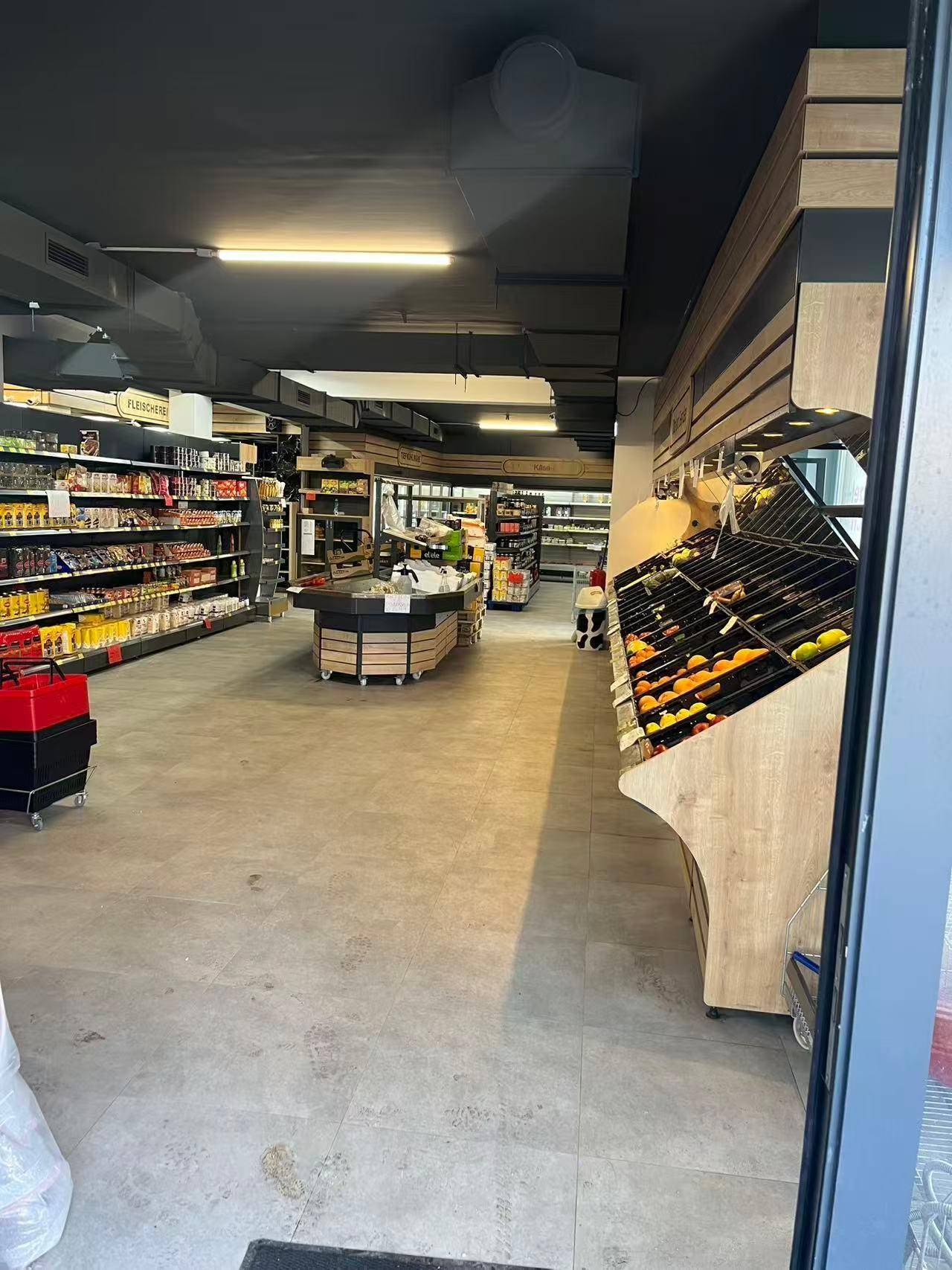 Langer Gang eines Ladengeschäfts mit Obstauslage, Regalen voller Waren und Fliesenboden.