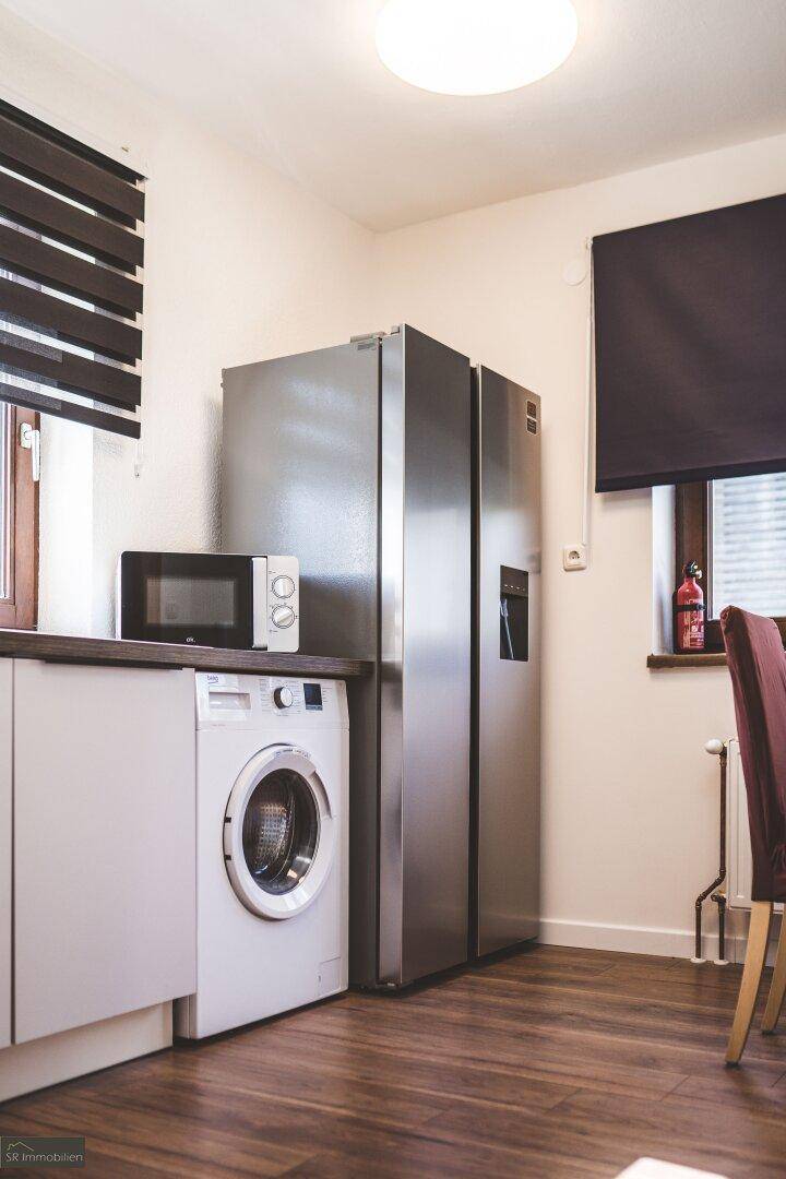 Detailansicht der Küche mit großem Kühlschrank, Mikrowelle und Waschmaschine.