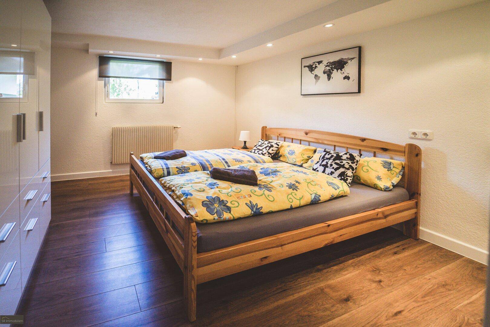 Schlafzimmer mit hellem Holzbett, Holzboden und weißem Kleiderschrank, modern eingerichtet.