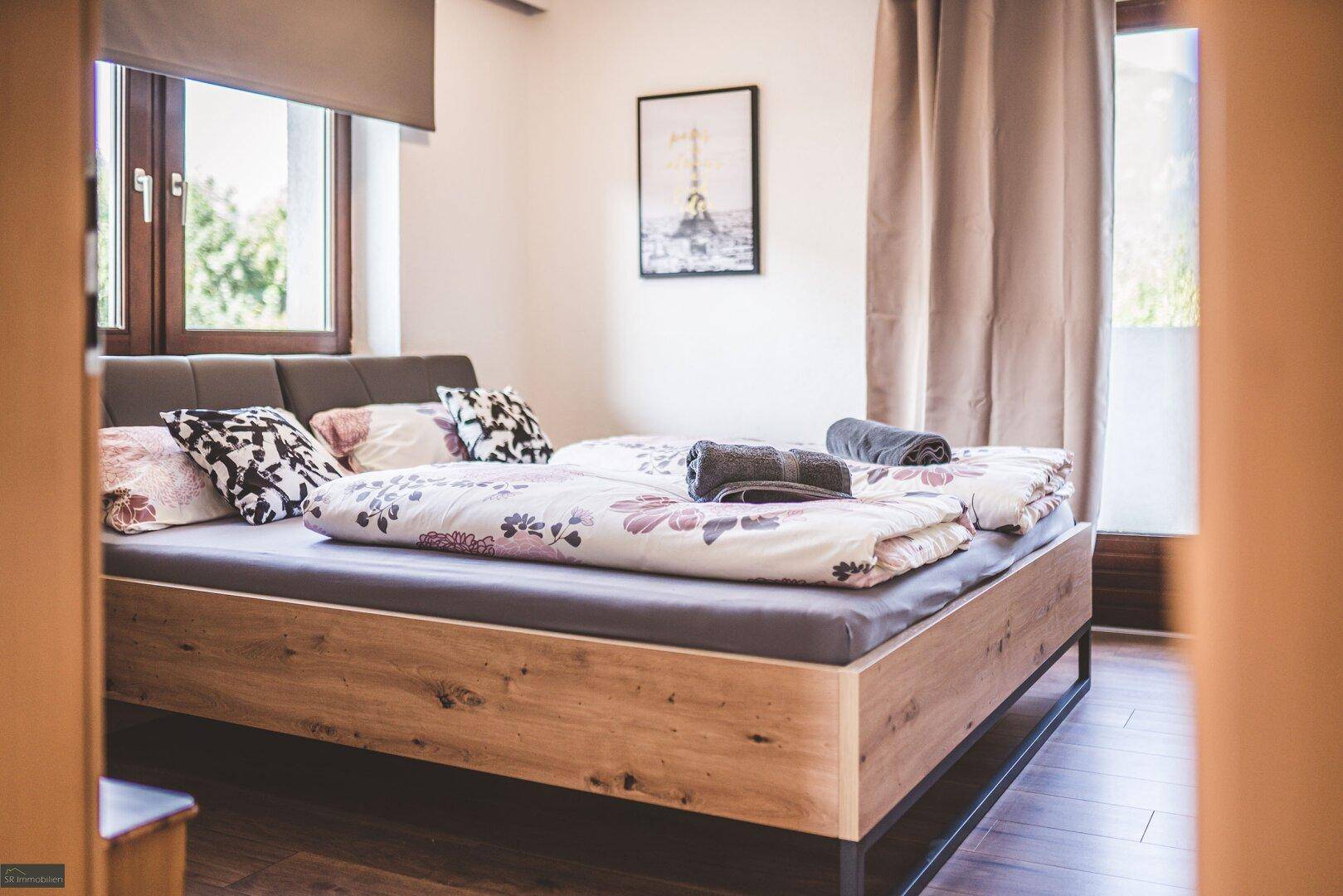 Helles Schlafzimmer mit Doppelbett, Holzboden und Blick ins Grüne durch das Fenster.