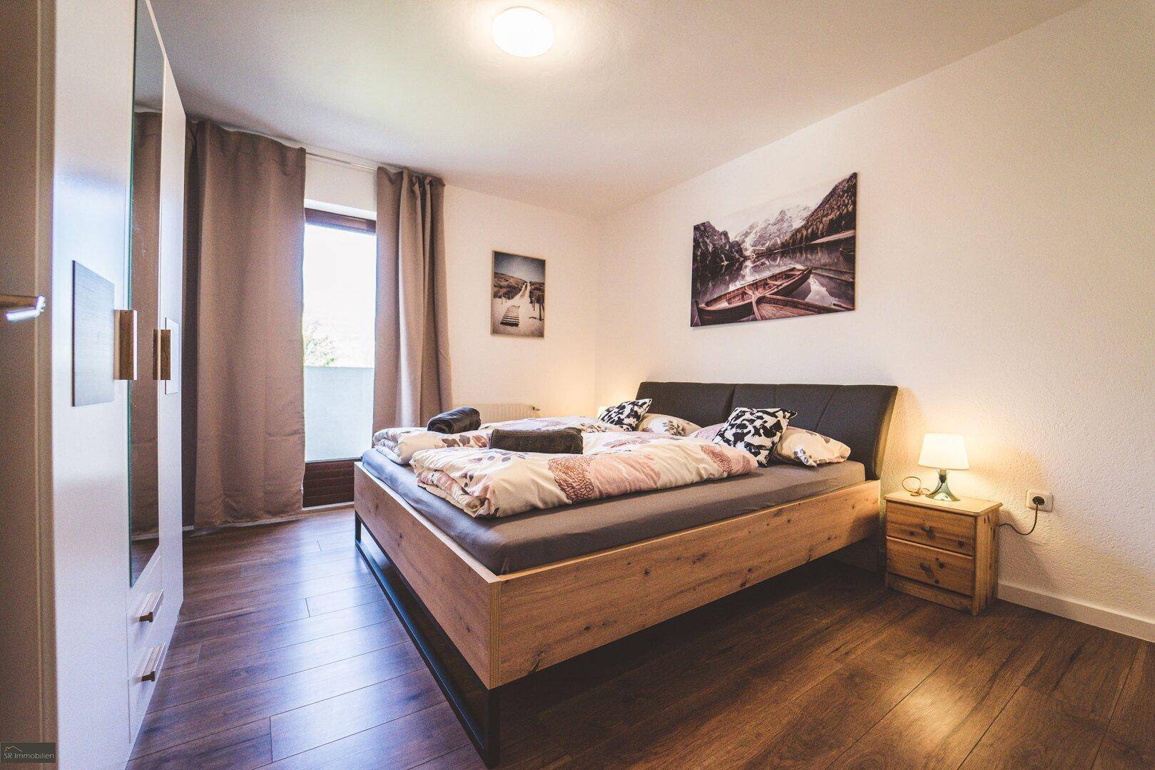 Schlafzimmer mit Doppelbett, Holzboden und Zugang zu einem Balkon, hell und einladend.