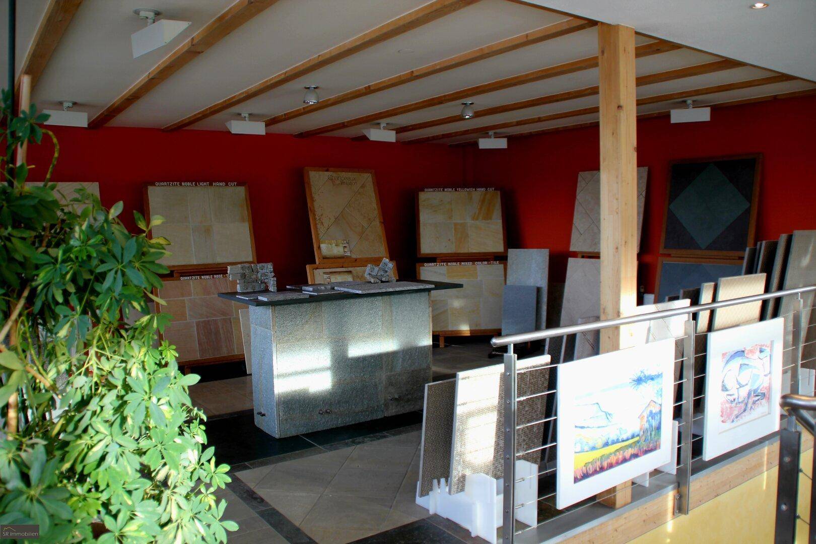 Geräumiger Ausstellungsraum mit verschiedenen Steinplatten, roten Wänden und sichtbaren Deckenbalken.