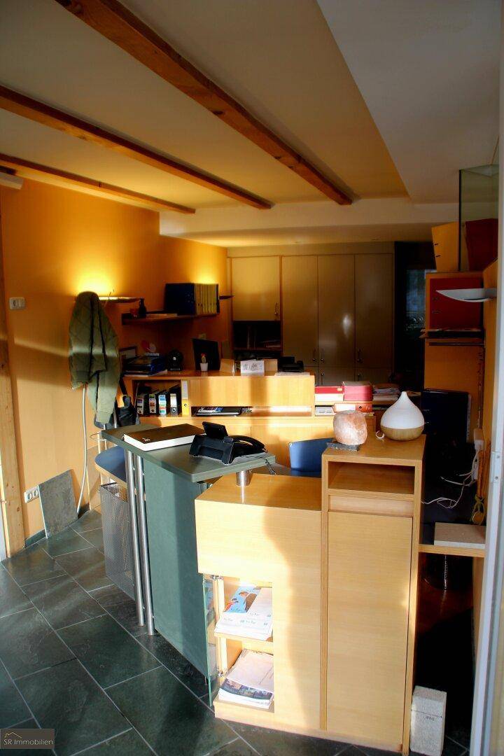 Empfangsbereich oder Büro mit Holzmöbeln, dunklen Fliesen und sichtbaren Deckenbalken.