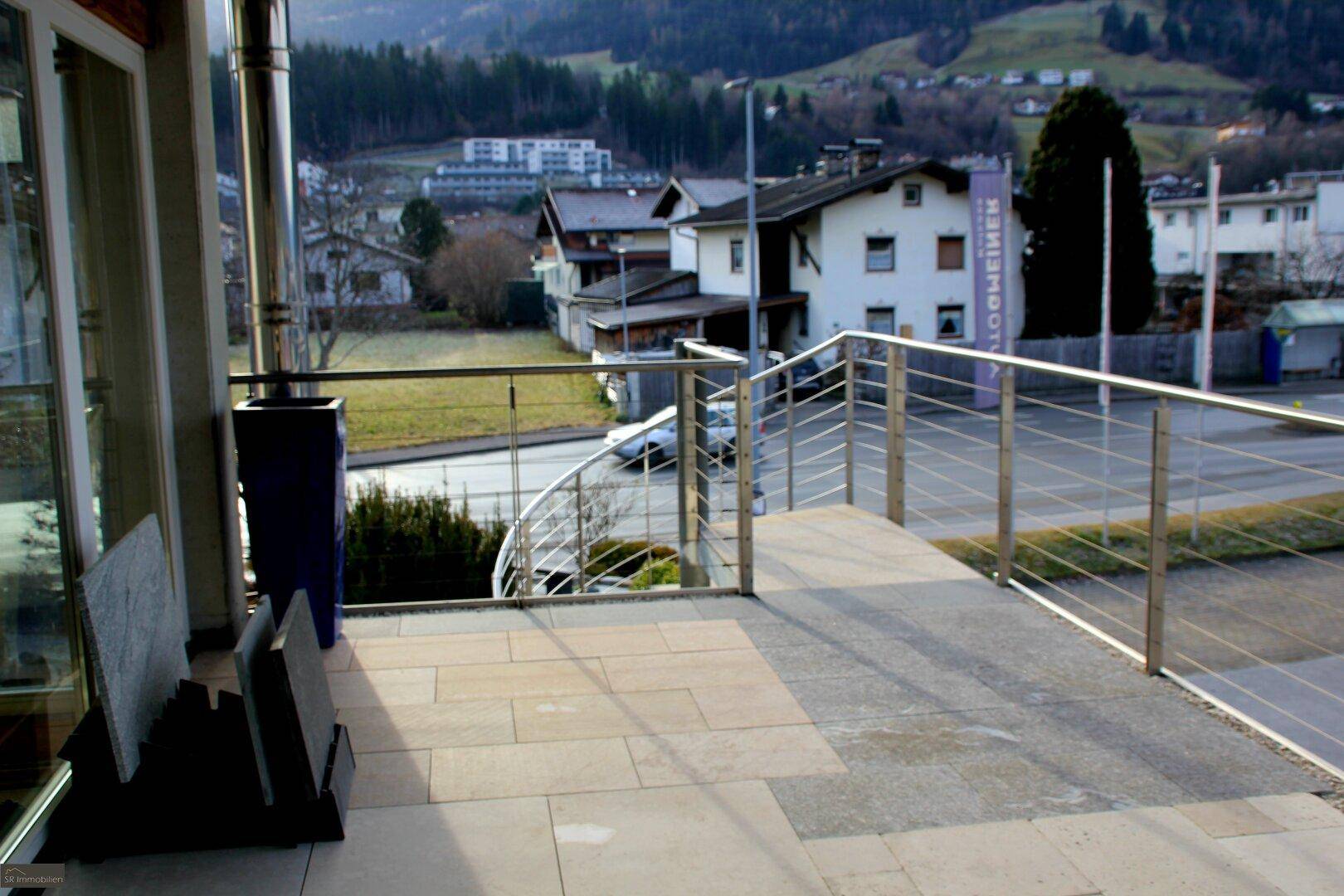 Geräumige Terrasse mit Steinplatten und Edelstahlgeländer, bietet Blick auf die Umgebung und Häuser.