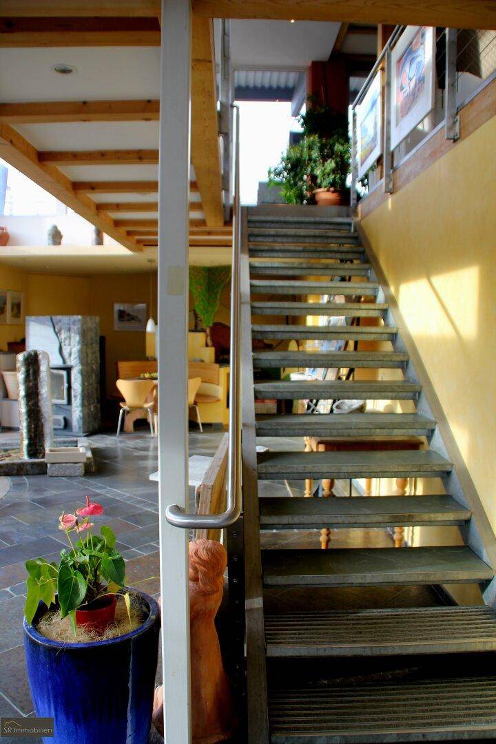 Innenbereich mit moderner Treppe aus Metall und Holz, führt zu einer oberen Etage mit sichtbaren Balken.
