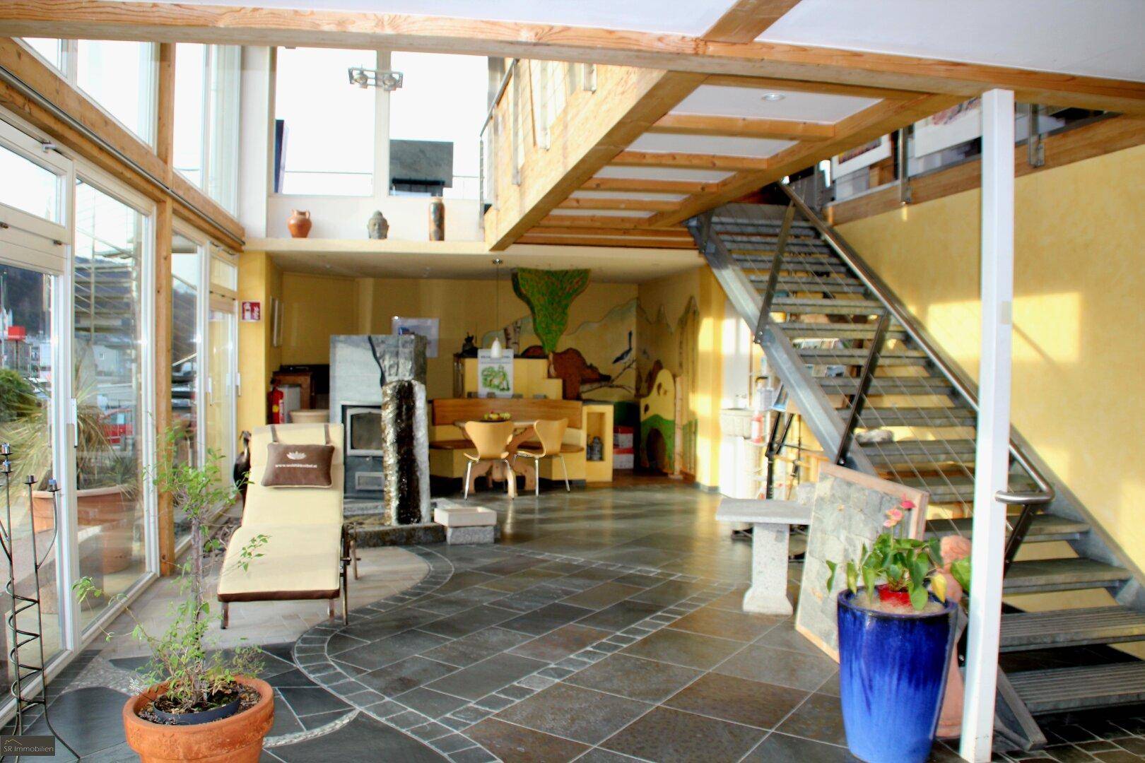 Offener Empfangsbereich mit hoher Decke, Treppe, Kamin und dekorativen Elementen, hell und geräumig.