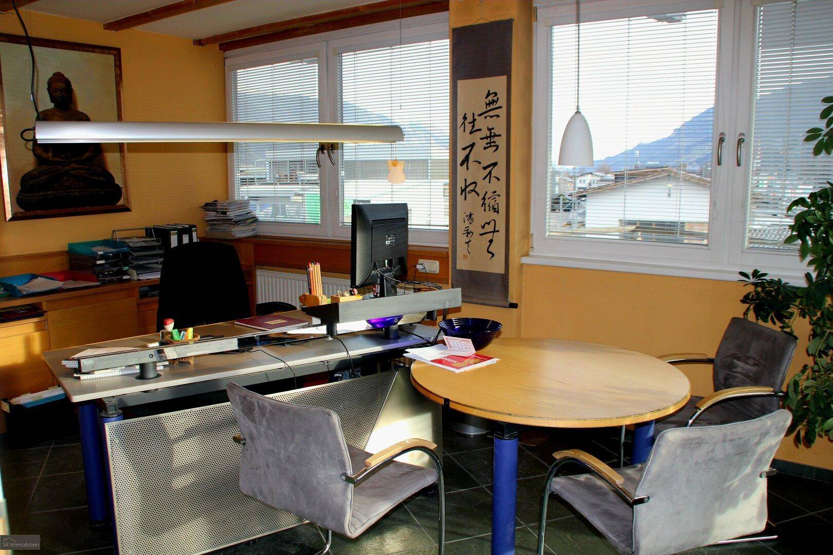 Helles Büro mit Schreibtisch, Besprechungstisch und Blick auf die umliegende Landschaft und Berge.