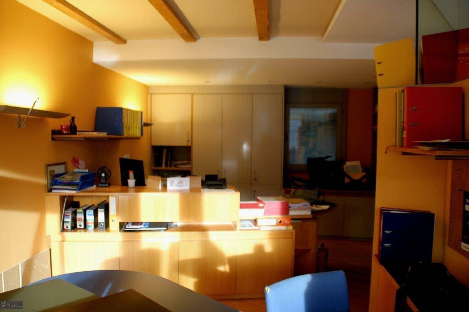 Büro mit Holzmöbeln, Regalen und warmem Licht, teilweise mit sichtbaren Deckenbalken und Stauraum.