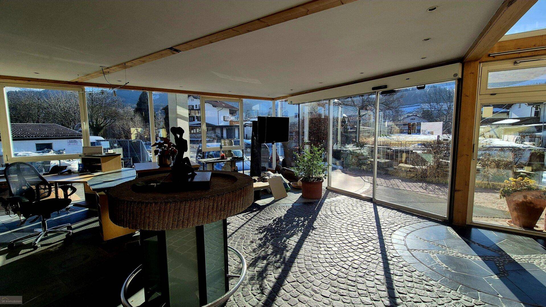Geräumiger Showroom mit runder Theke, Pflanzen und einer beeindruckenden Glasfassade, die viel Licht hereinlässt.
