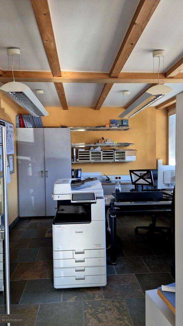 Detailansicht eines Bürobereichs mit Drucker, Regalen und sichtbaren Holzbalken an der Decke.