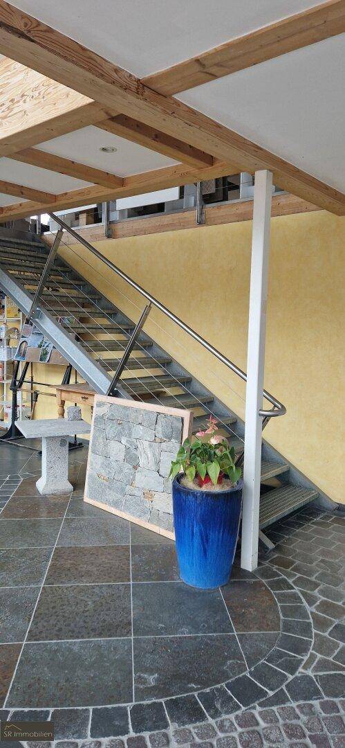 Moderne Treppe mit Metallgeländer und Steinfußboden in einem hellen, offenen Bereich.