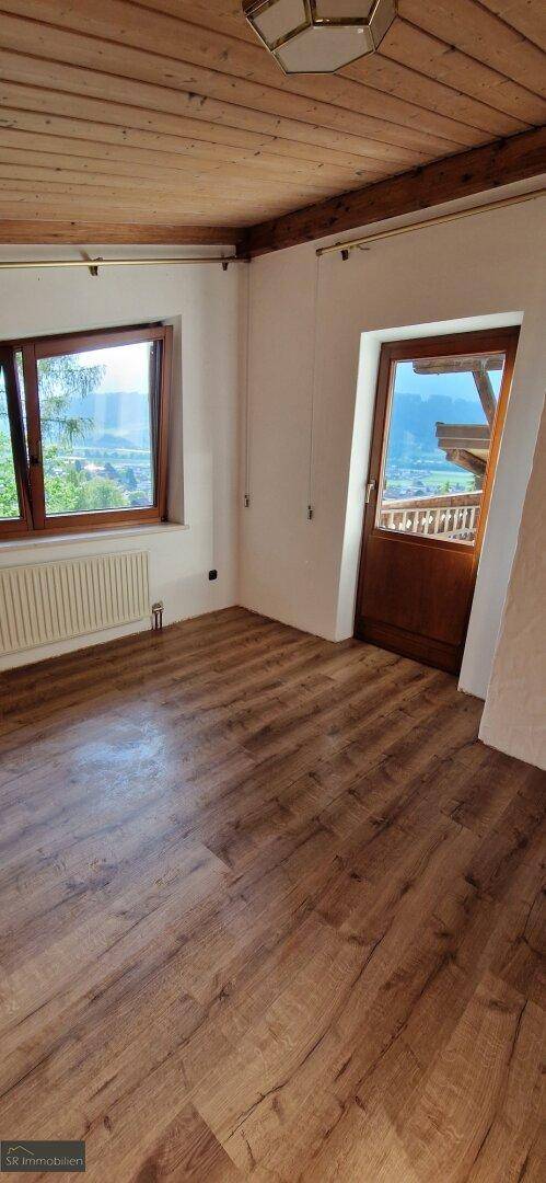 Heller Raum mit Laminatboden, Holzbalkendecke und Zugang zu einem Balkon mit Bergblick.