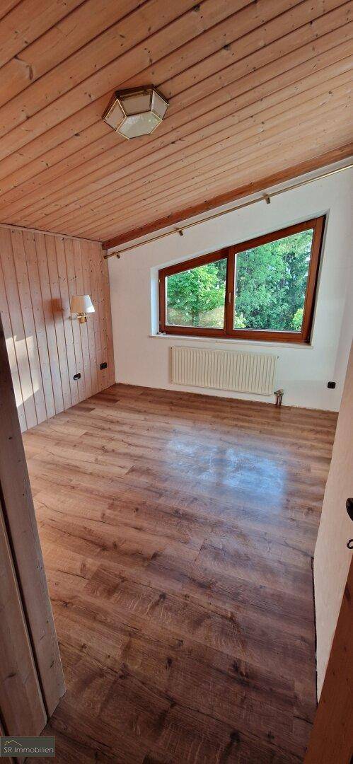 Gemütlicher Raum mit Laminatboden, Holzdecke und Fenster mit Blick ins Grüne.