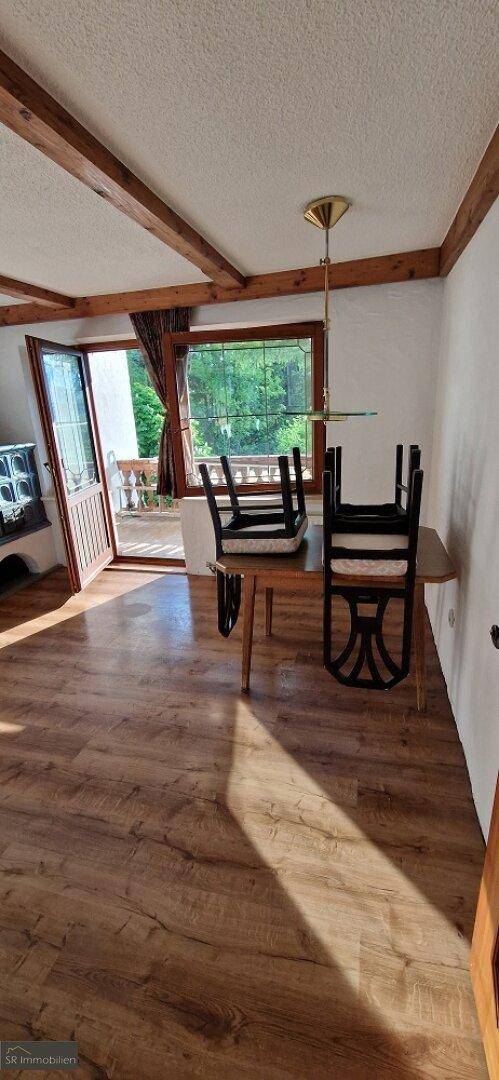 Essbereich mit Laminatboden, Holzbalkendecke und Zugang zu einem Außenbereich.