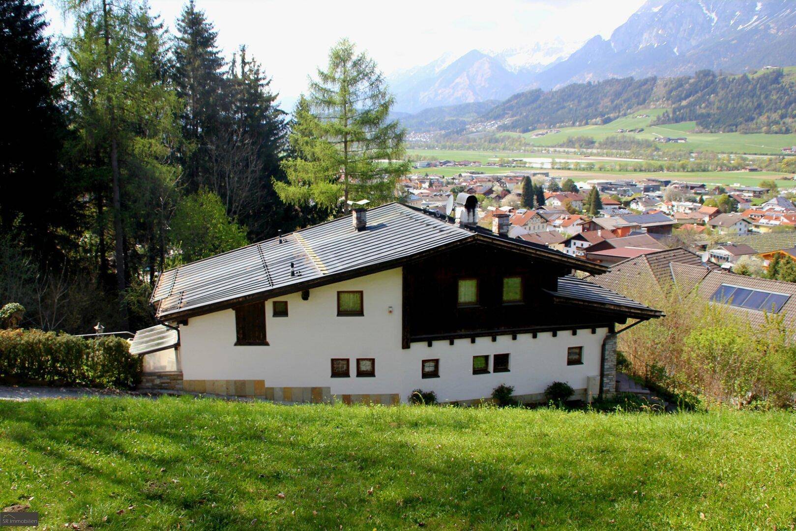 Traditionelles Haus mit weißer Fassade und dunklem Dach vor einer beeindruckenden Bergkulisse.