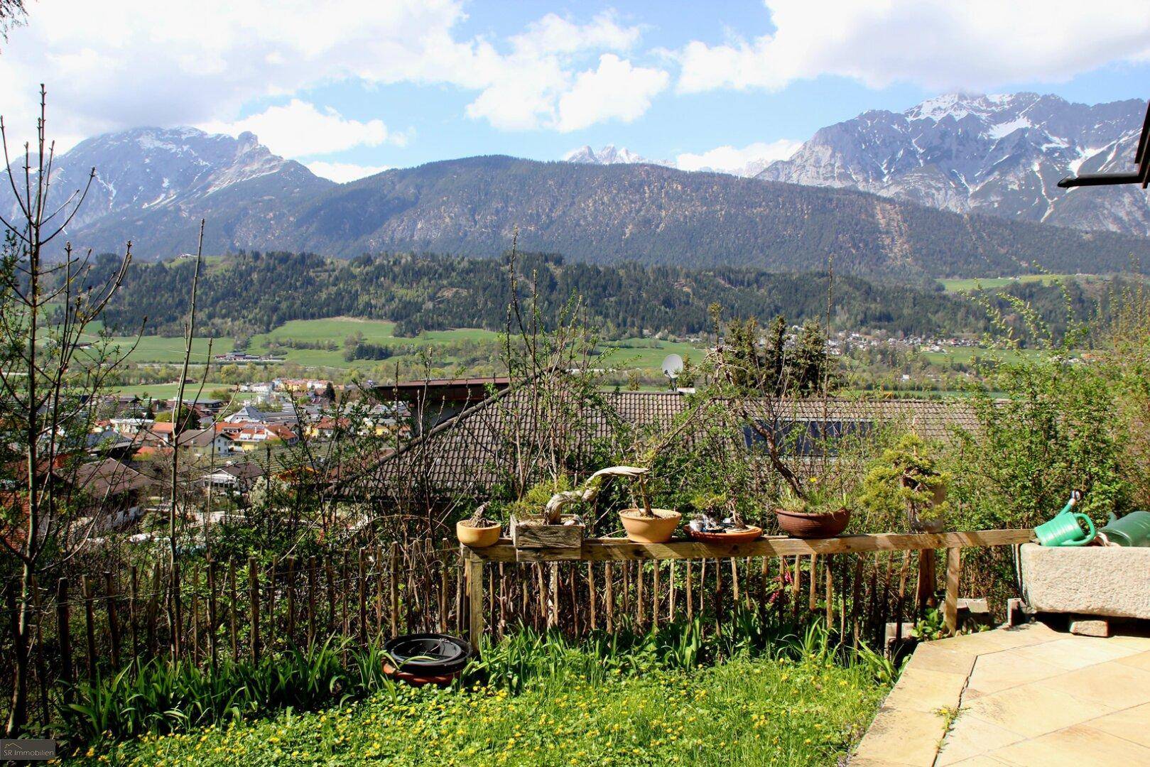 Grüner Gartenbereich mit Holzzaun und weitem Blick auf die umliegende Berglandschaft.