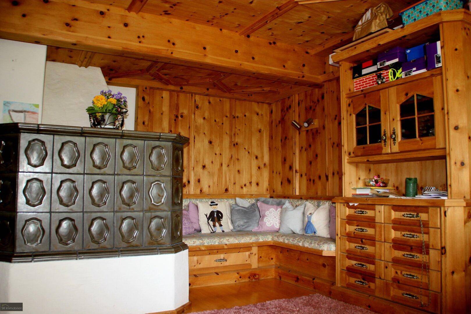 Rustikales Wohnzimmer mit traditionellem Kachelofen, Holztäfelung und gemütlicher Sitzecke.