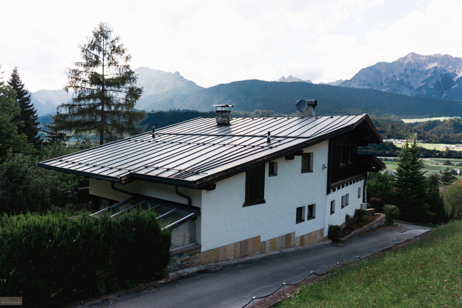 Seitenansicht des Hauses mit weißer Fassade und dunklem Dach, mit beeindruckendem Blick auf die umliegende Berglandschaft.
