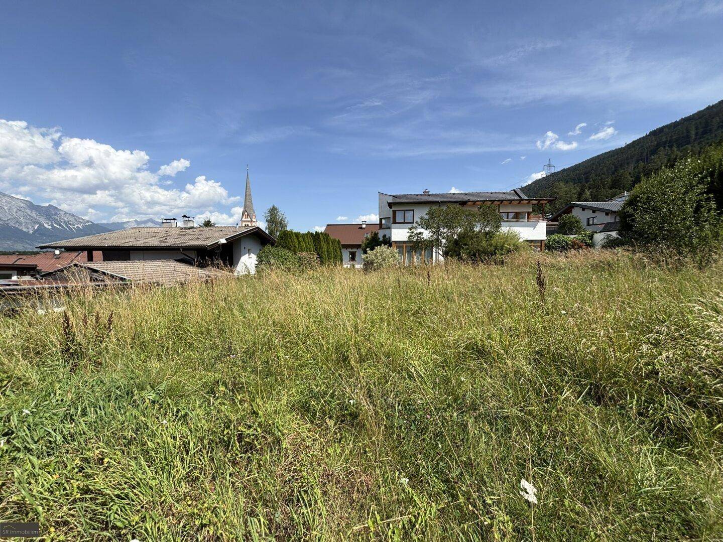 Weitläufiges, unbebautes Grundstück mit Panoramablick auf die Berge und eine nahegelegene Kirche.