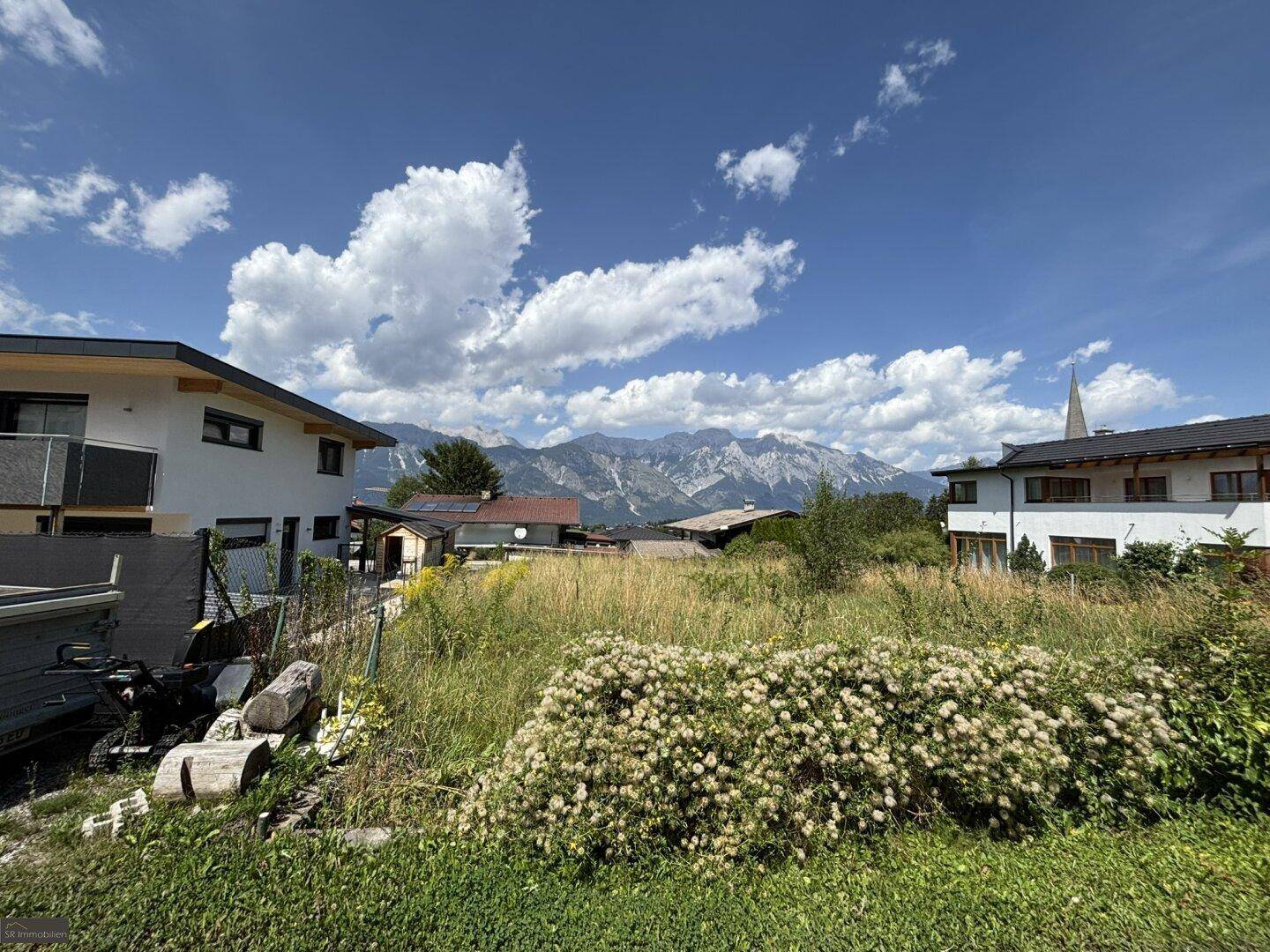 Sonniges Grundstück mit blühenden Sträuchern und einem weiten Blick auf die umliegende Bergwelt.