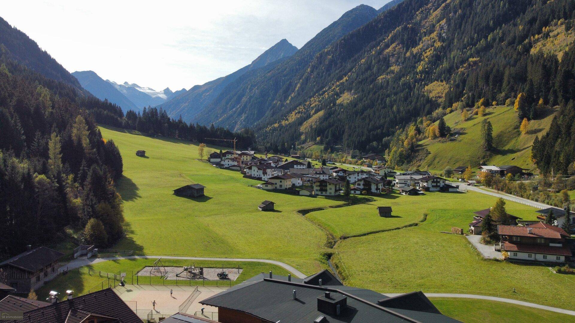 Weitläufige Ansicht eines malerischen Alpentals mit einem Dorf, grünen Wiesen und majestätischen Bergen.