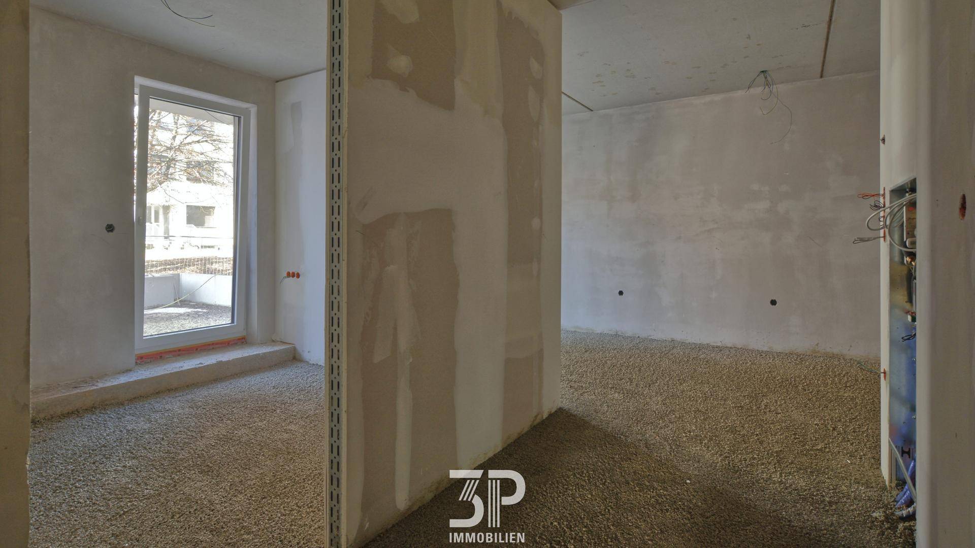 Rohbauzustand eines Innenraums mit großen Fenstern und vorbereitetem Boden für den Endausbau.