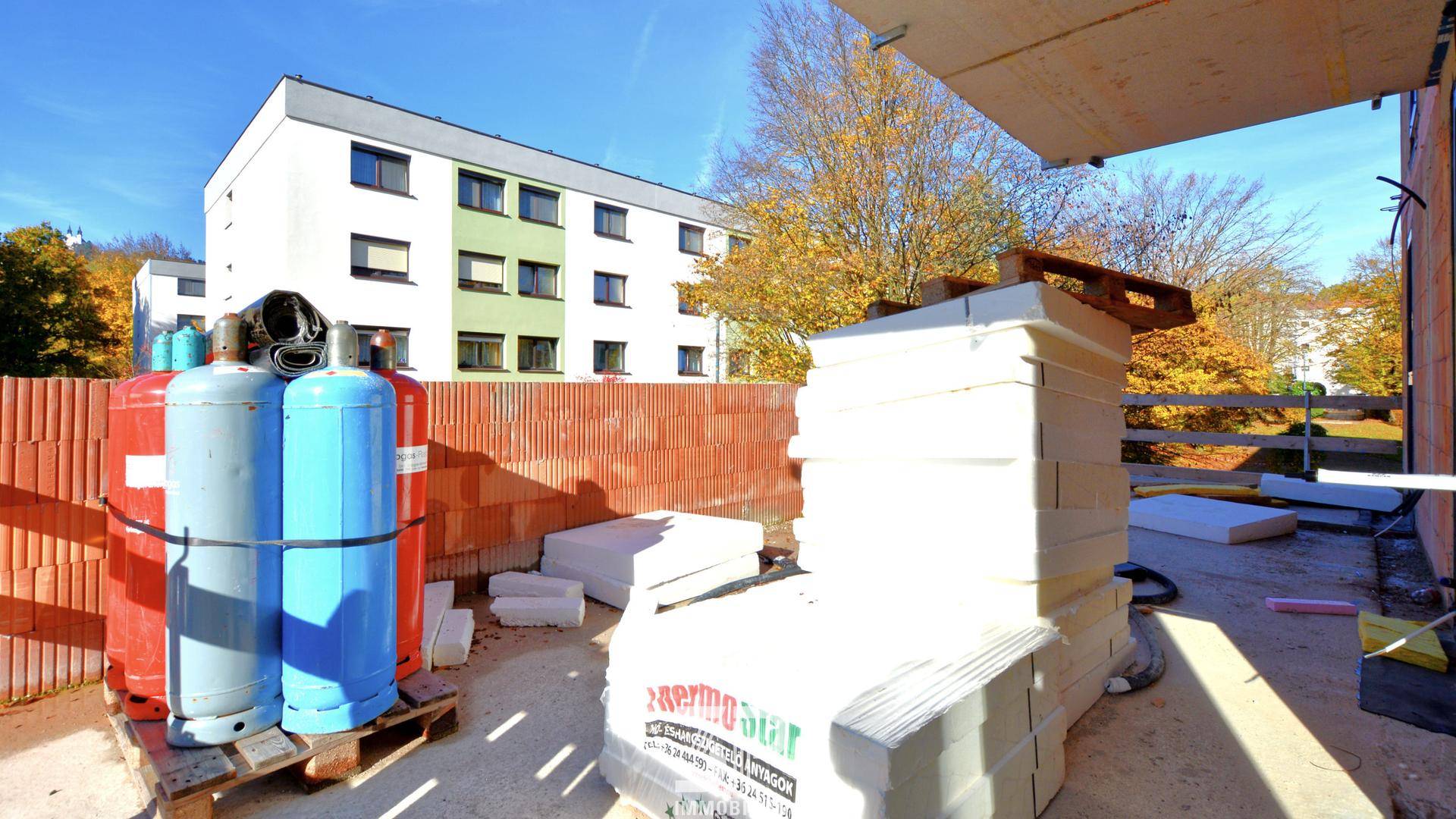 Baustelle mit Baumaterialien wie Gasflaschen und Dämmplatten vor einem Wohngebäude.